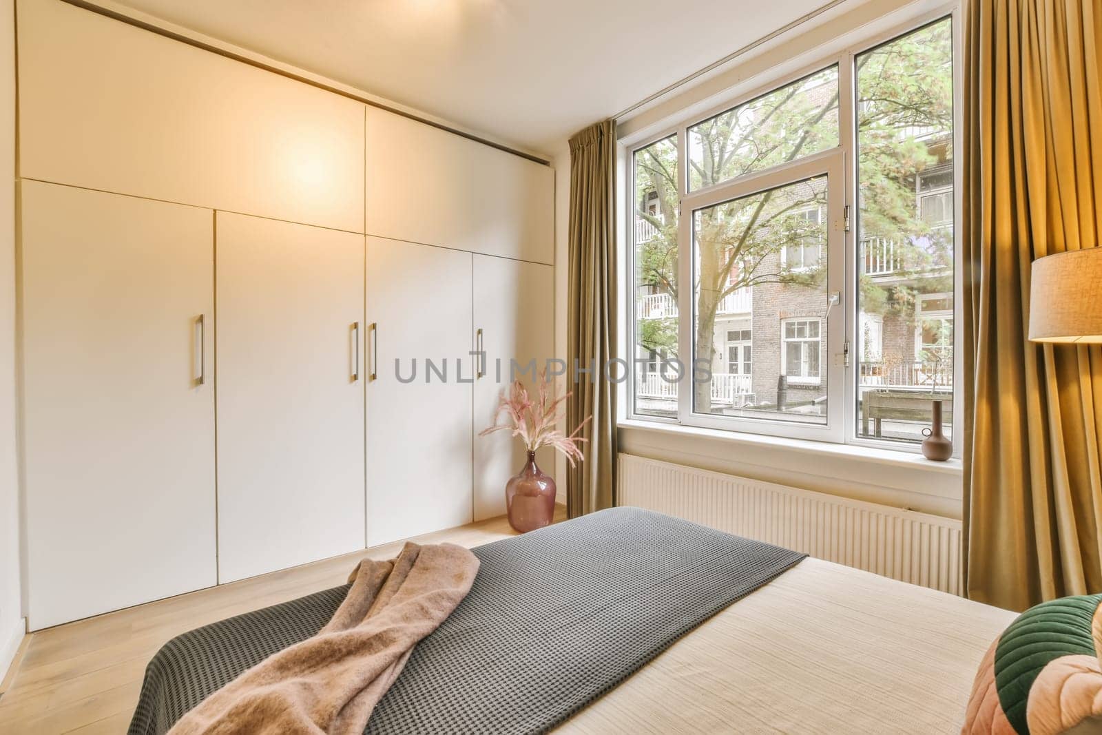 a bedroom with a bed and wardrobes in front of a large window that has curtains on the outside wall
