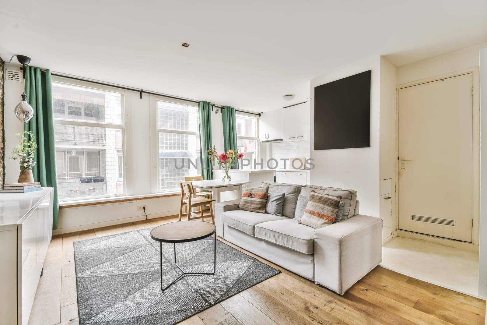 a living room with wood flooring and green drapes hanging on the wall behind it is a white couch