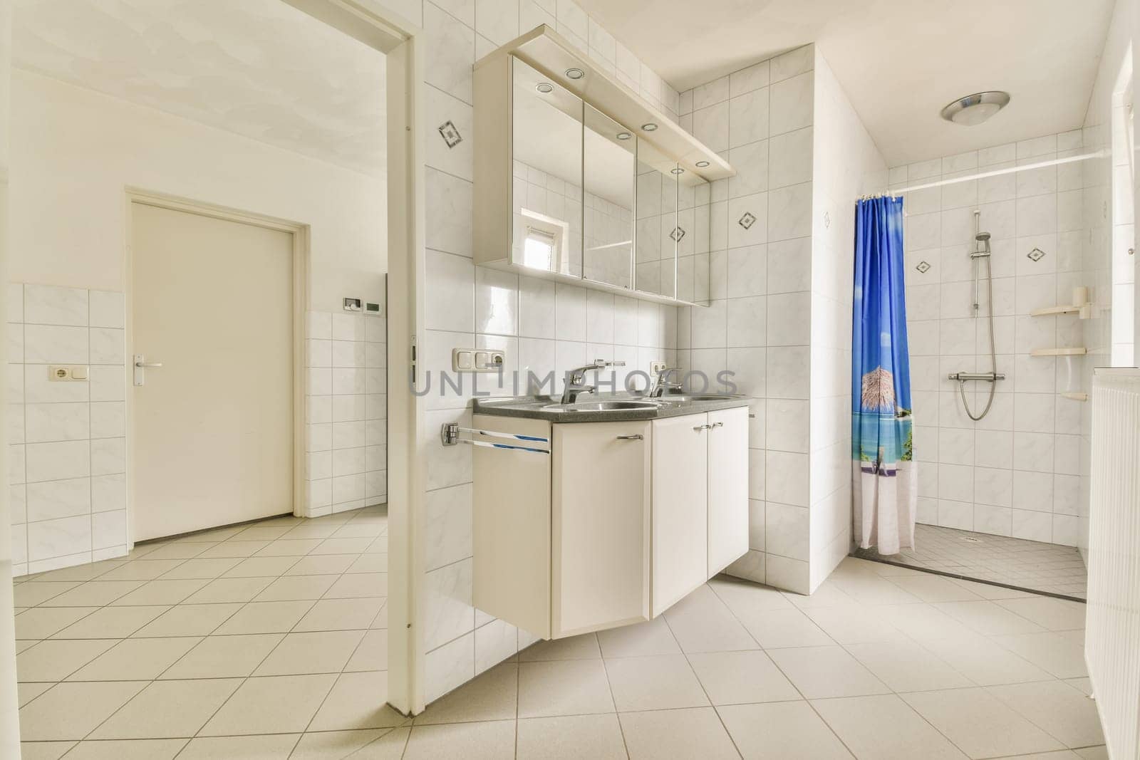 a bathroom with white tile and blue shower curtain on the window simng it's in front of the sink
