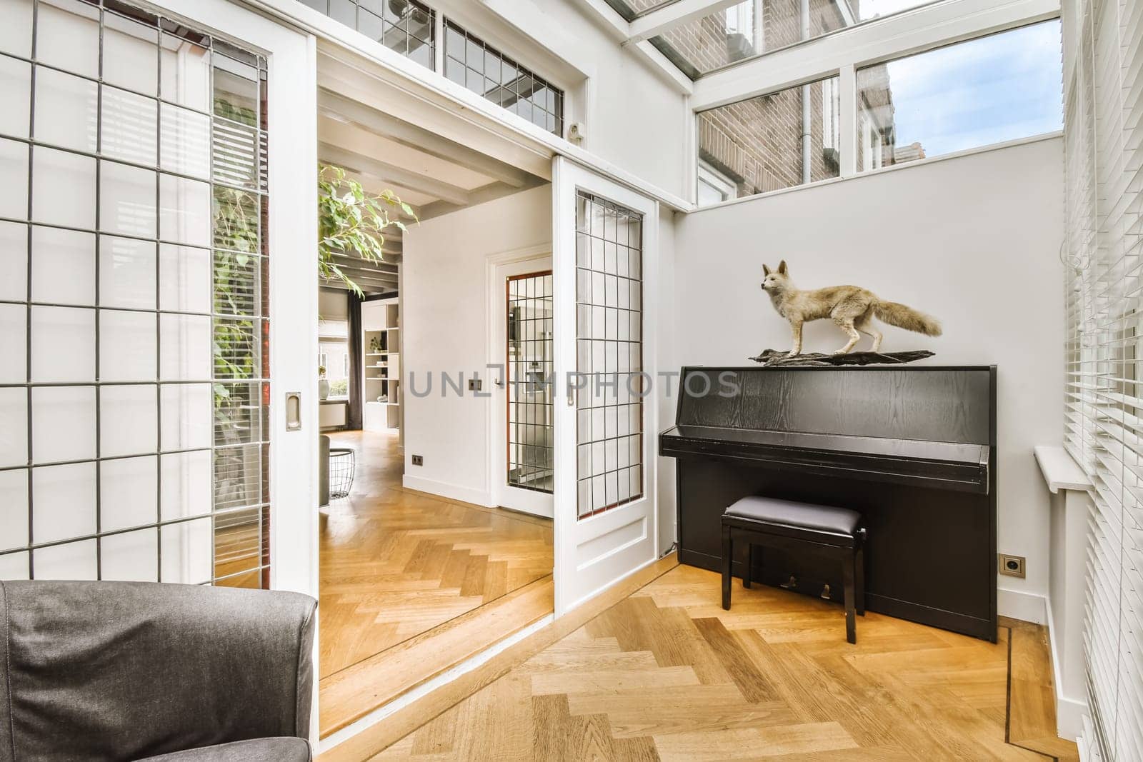 a cat sitting on top of a piano in a living room with wood flooring and white brick wall behind it