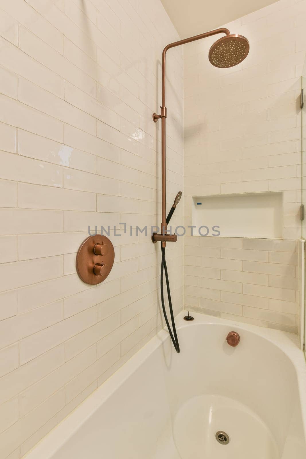 a bathtub and shower head in a bathroom with white tiles on the wall behind it is a shelf for books