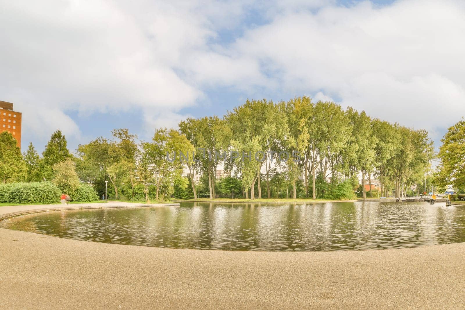 a pond in the middle of a city park with trees and buildings on both sides, as seen from the water's edge