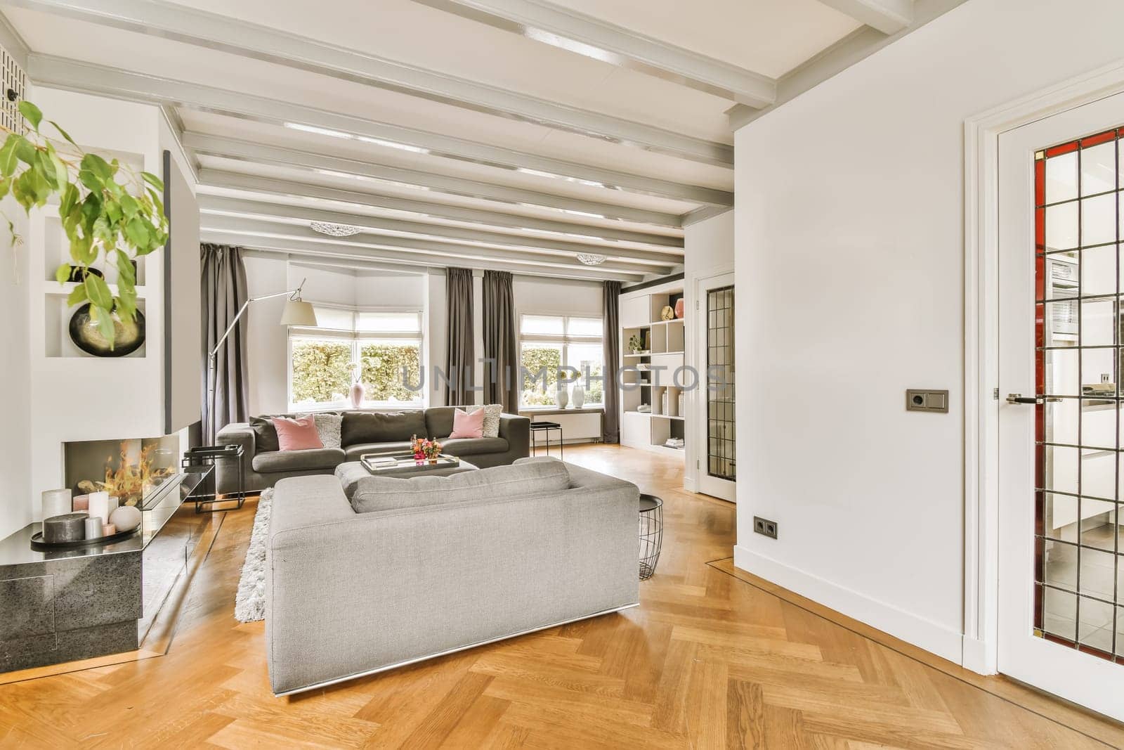 a living room with wood flooring and white walls in the center of the room is a grey couch, coffee table, mirror