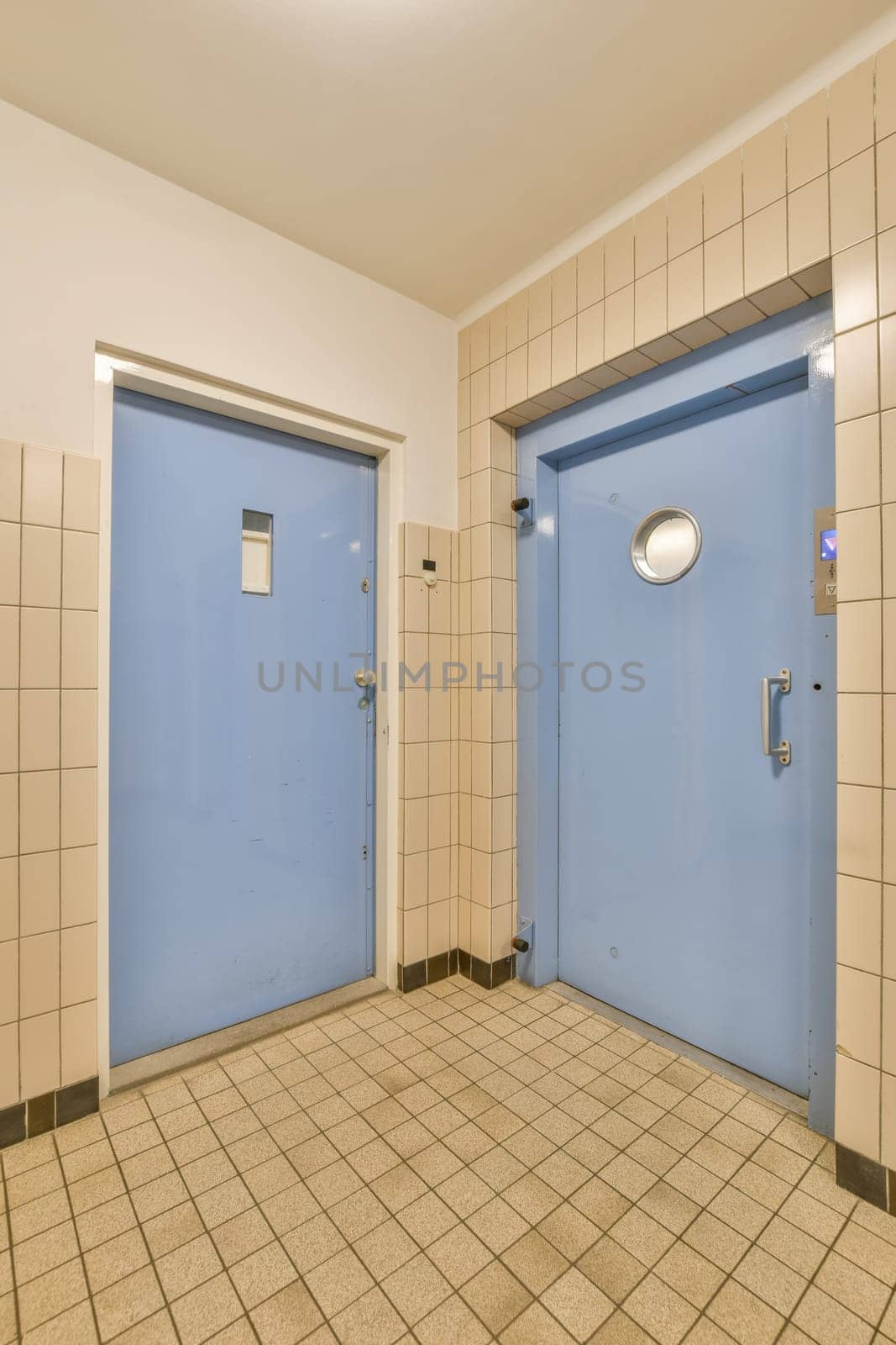 two blue doors in an empty room with tiled floor and white tiles on the walls, one door is open