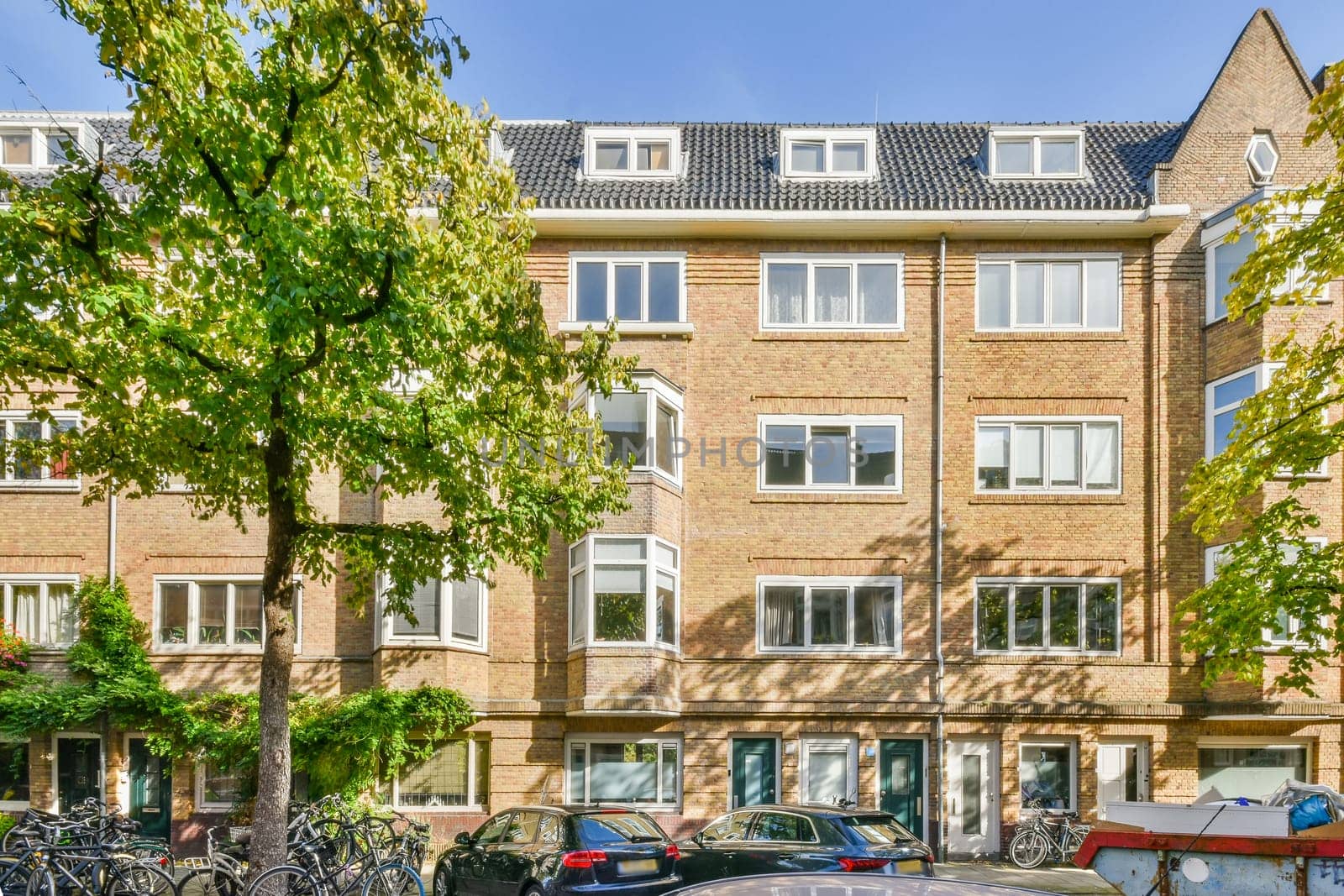 an apartment complex in the netherlands, with bikes parked on the street and cars parked along the curbed road