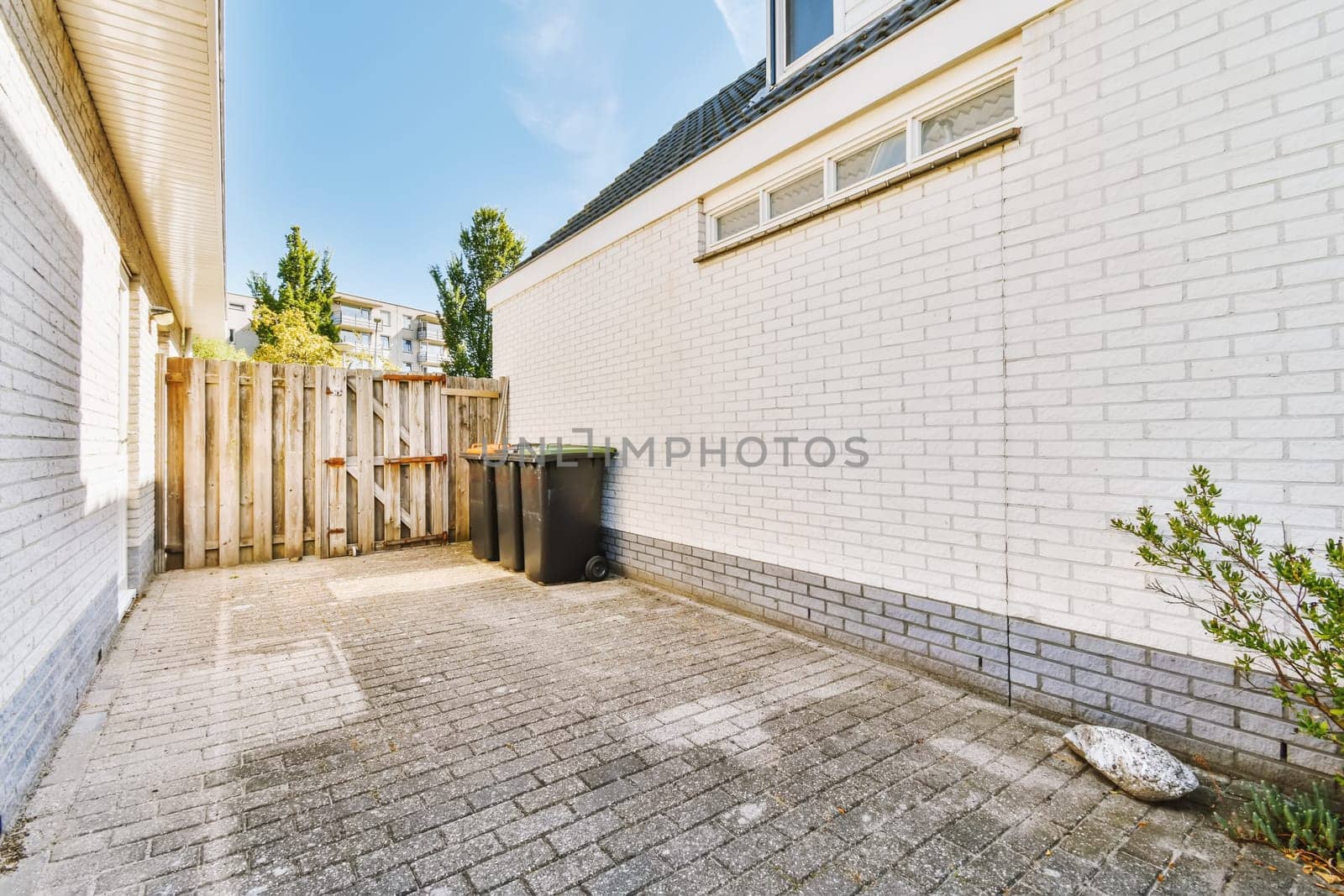 an empty back yard with white brick walls and green trees in the area is surrounded by grey bricks, blue sky