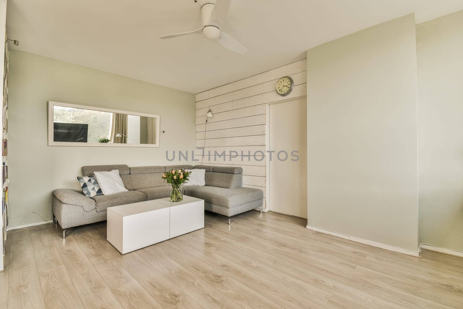 a living room with wood flooring and white paint on the walls, ceiling fan is mounted above the couch