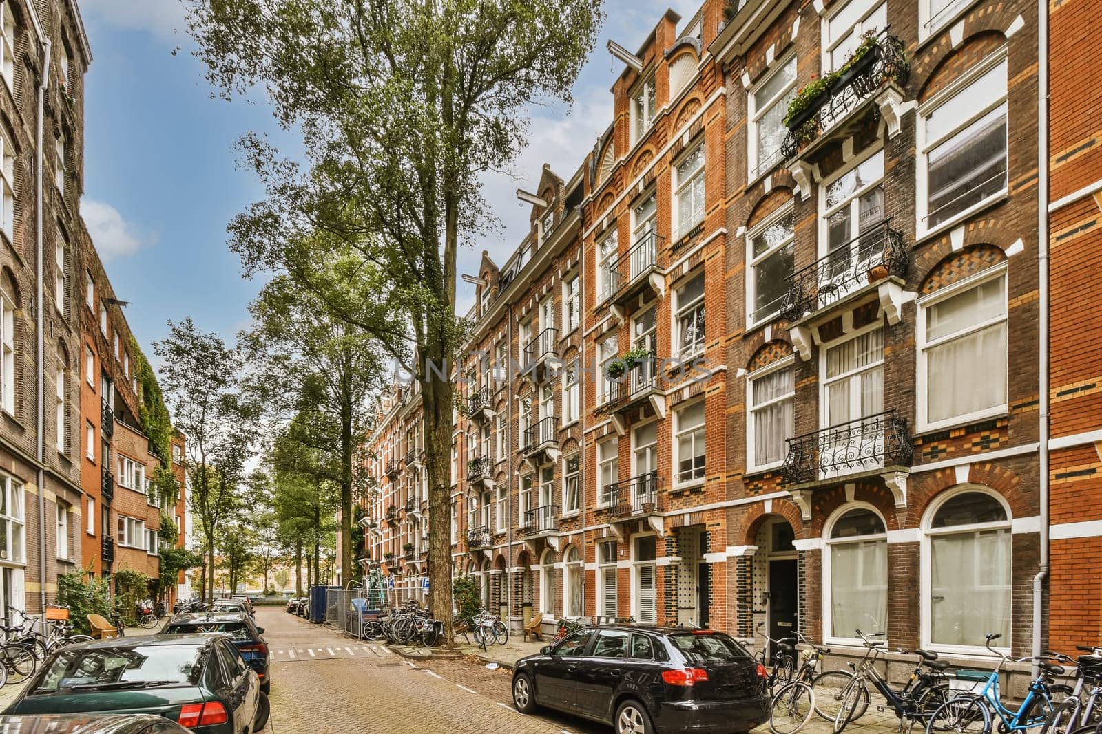 some cars parked on the side of a street in an urban area with many bricked buildings and trees lining both sides