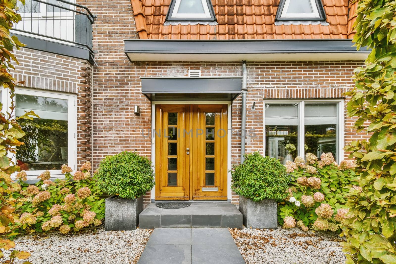 the front entrance to a house with plants and flowers in pots on either sides, surrounded by red brick walls
