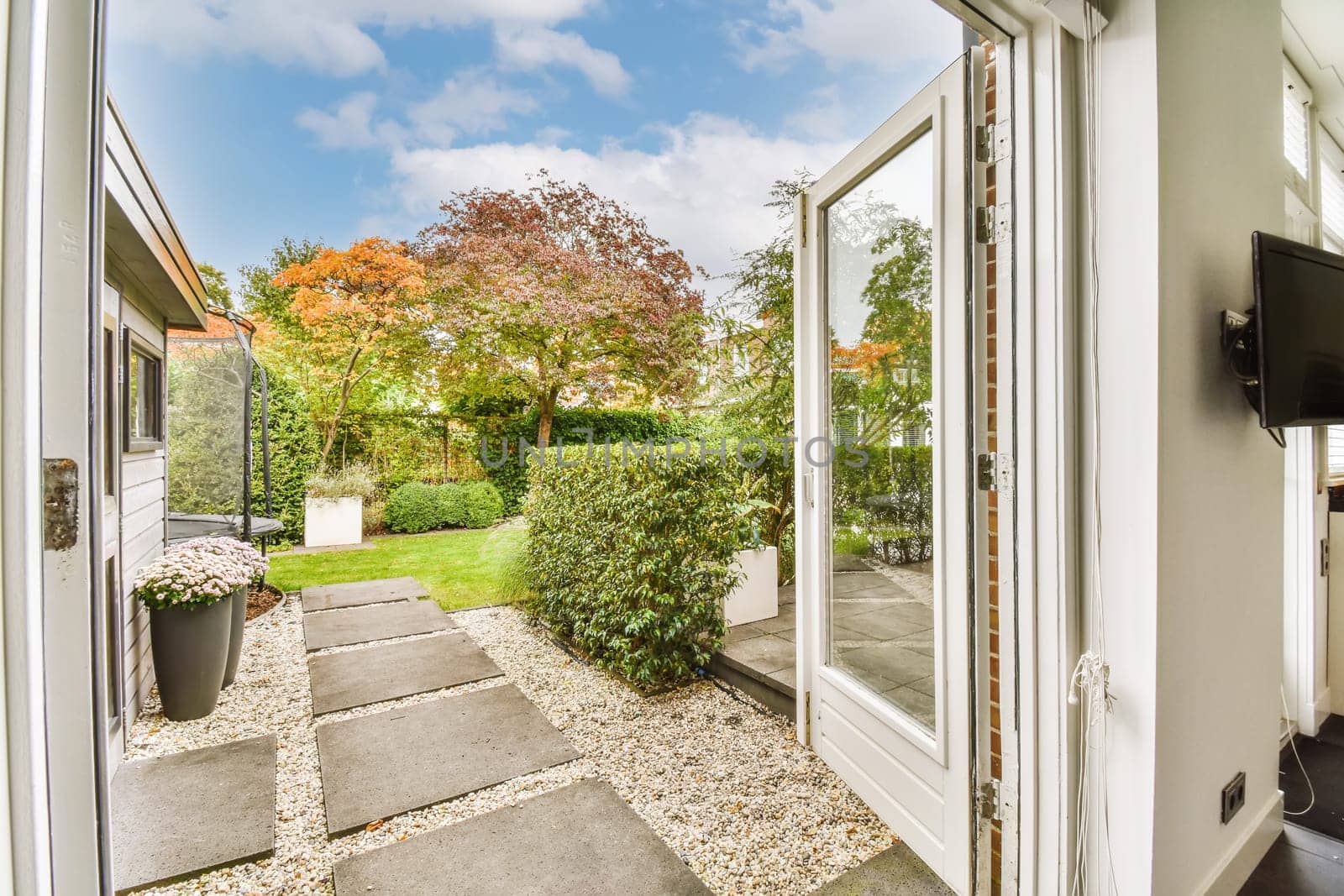 the outside of a house from inside an open door looking out onto a garden with trees and bushes in the background