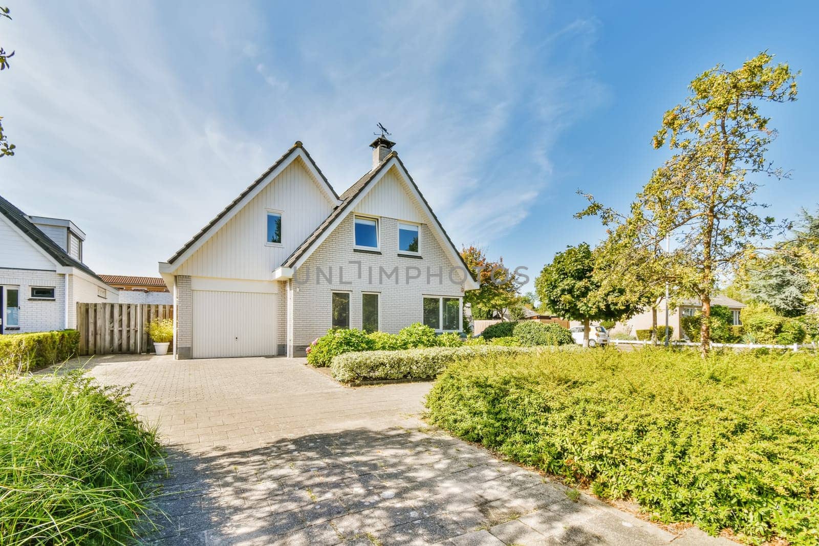 a house with white sidings and blue sky in the background there is a driveway leading up to the front door