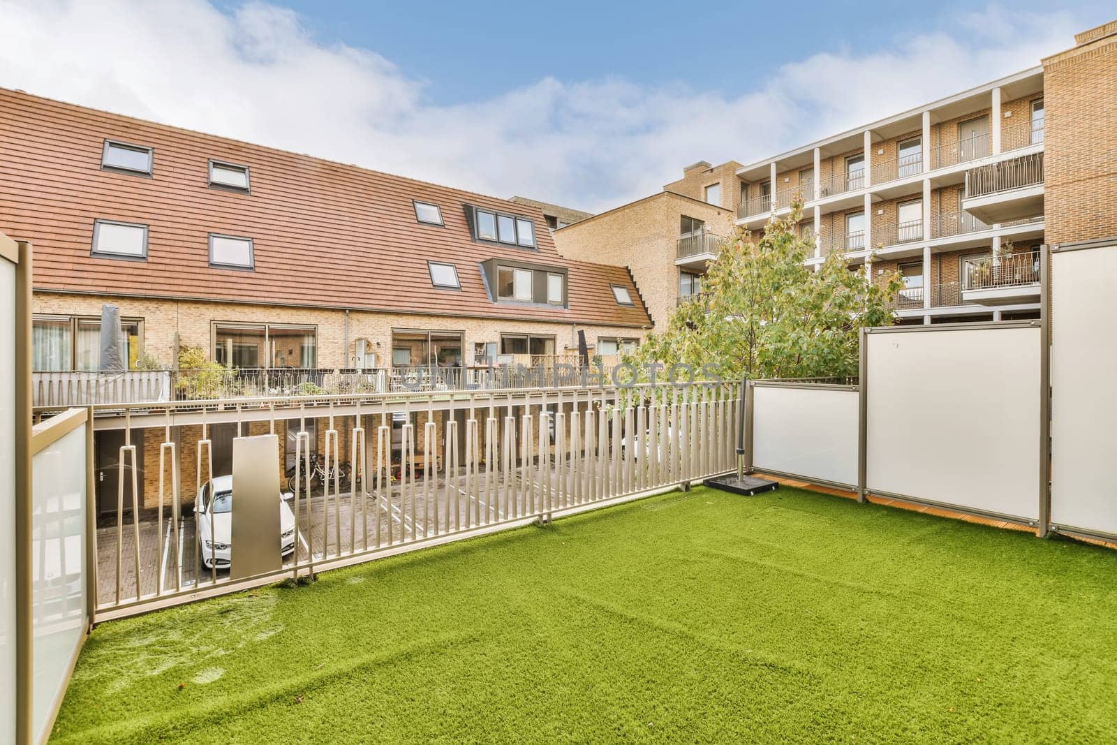 an outside area with green grass and white fenced in to the back of a two story brick apartment building