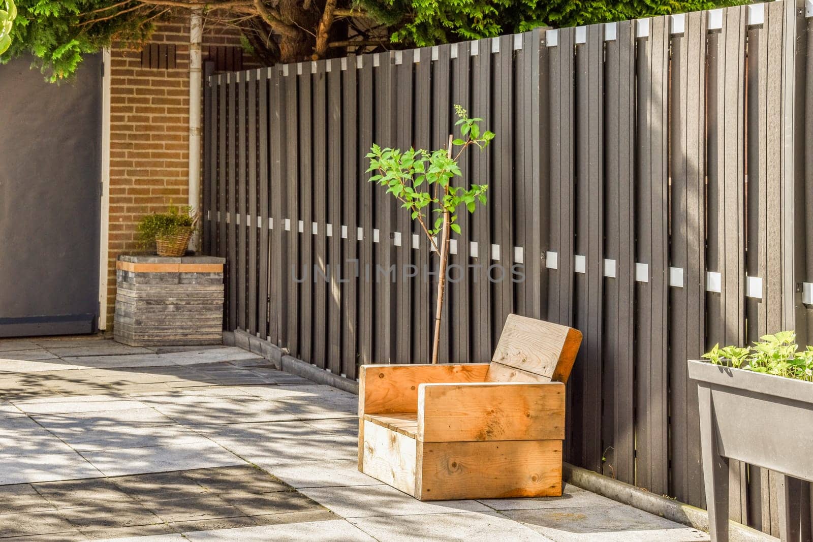 a small tree growing in a box on the sidewalk next to a wooden fence that has been painted with white paint