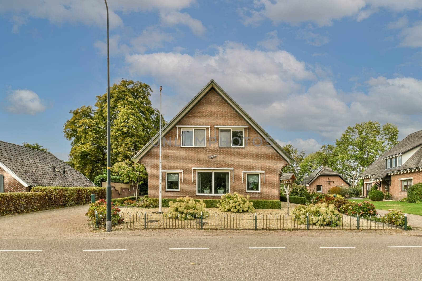 a house that is in the middle of a residential area with trees and bushes on either side of the street