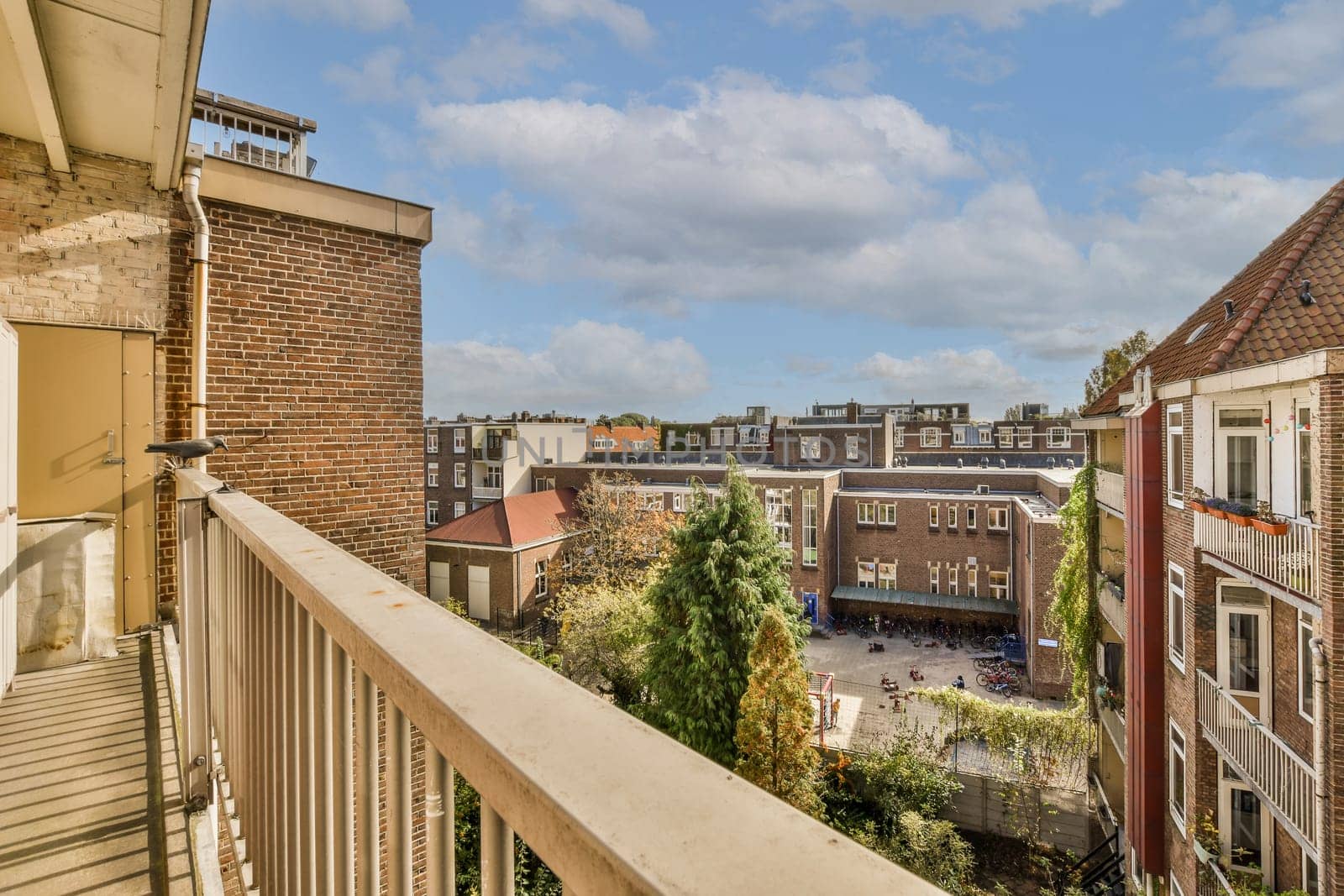 a balcony with some buildings in the background and blue sky above it, as seen from an apartment building window