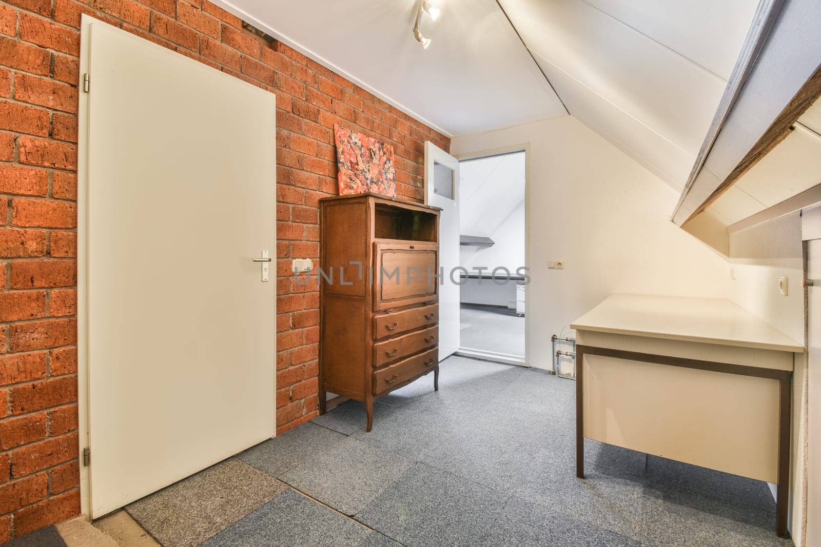 a room with a brick wall and an open white door in the center of the room is a small desk