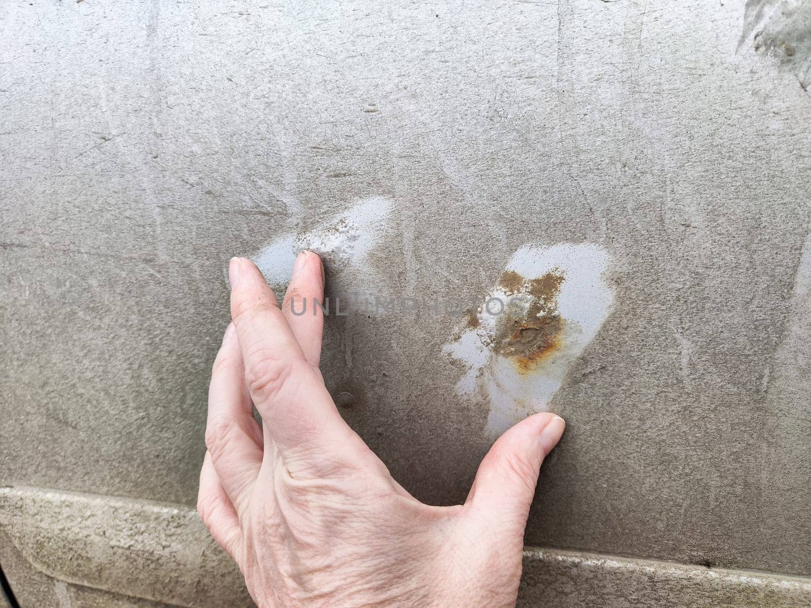 A hand rests on a dirty car surface, highlighting the contrast between the unclean areas and the untouched spots. This moment emphasizes vehicle care.
