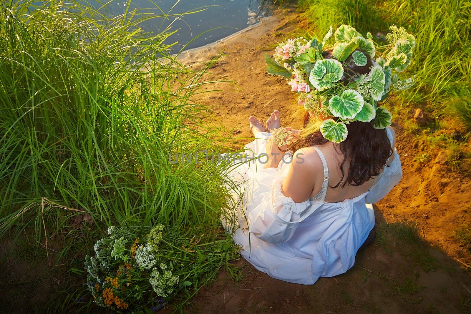 Slavic plump chubby girl in long white dress on the feast of Ivan Kupala with flowers and water in a river or lake on summer evening