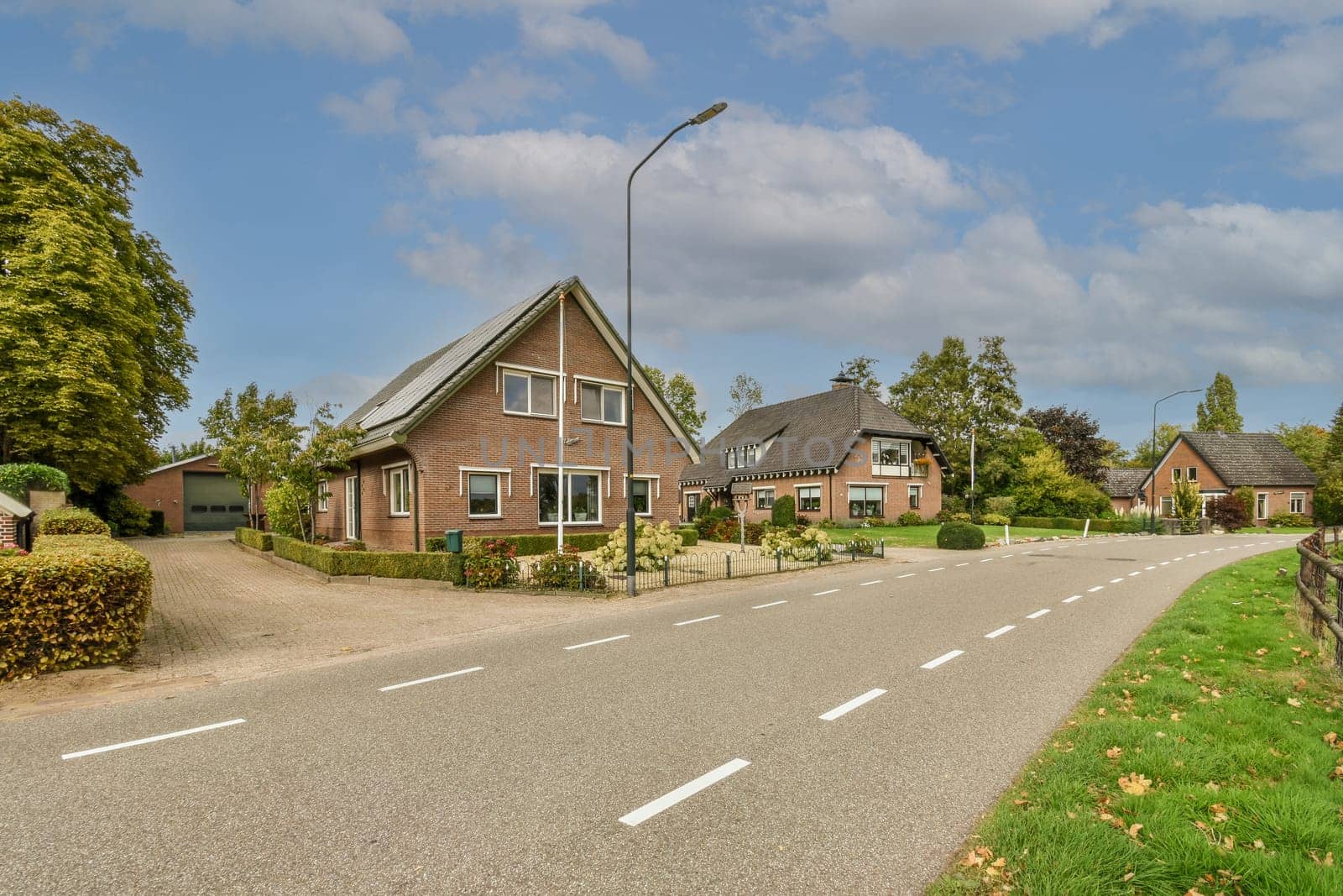 a street with houses in the background and trees on both sides, along an empty road that leads to a parking lot