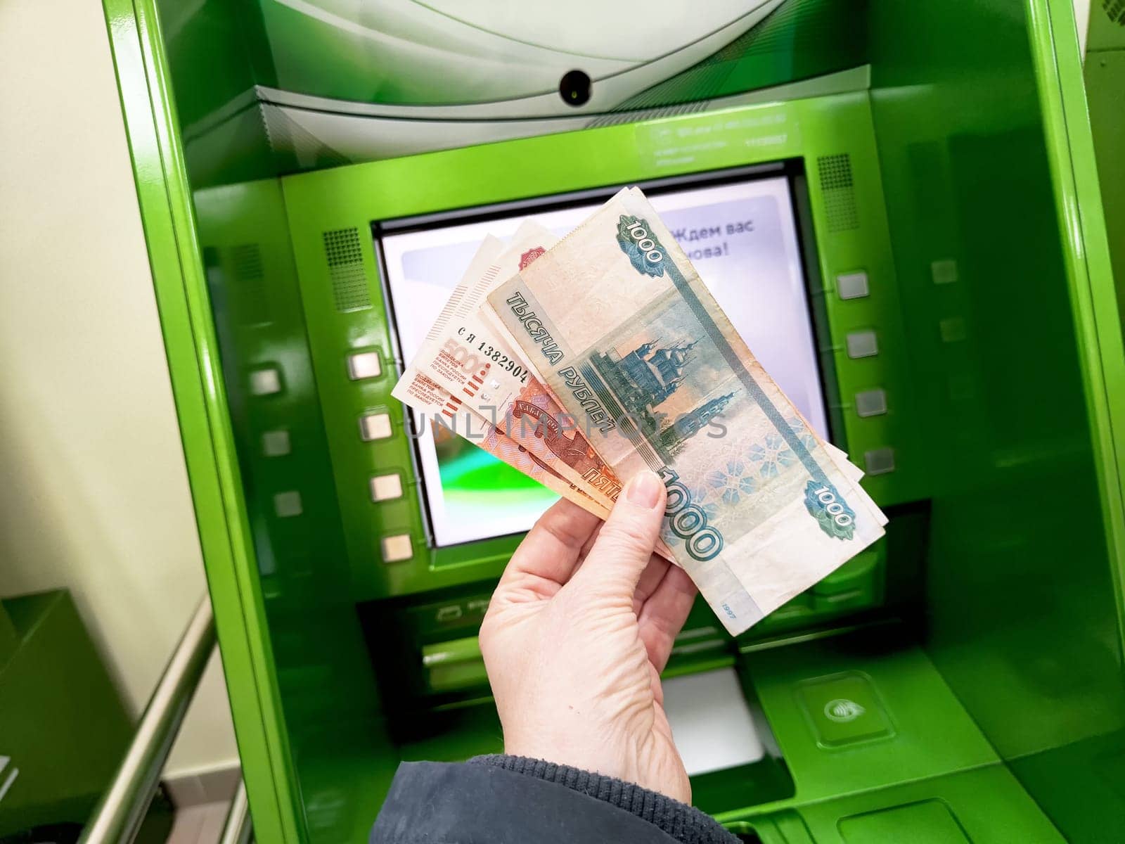 Kirov, Russia - March 15, 2025: Banknotes are being counted in front of a digital ATM screen at a banking location during daylight hours.