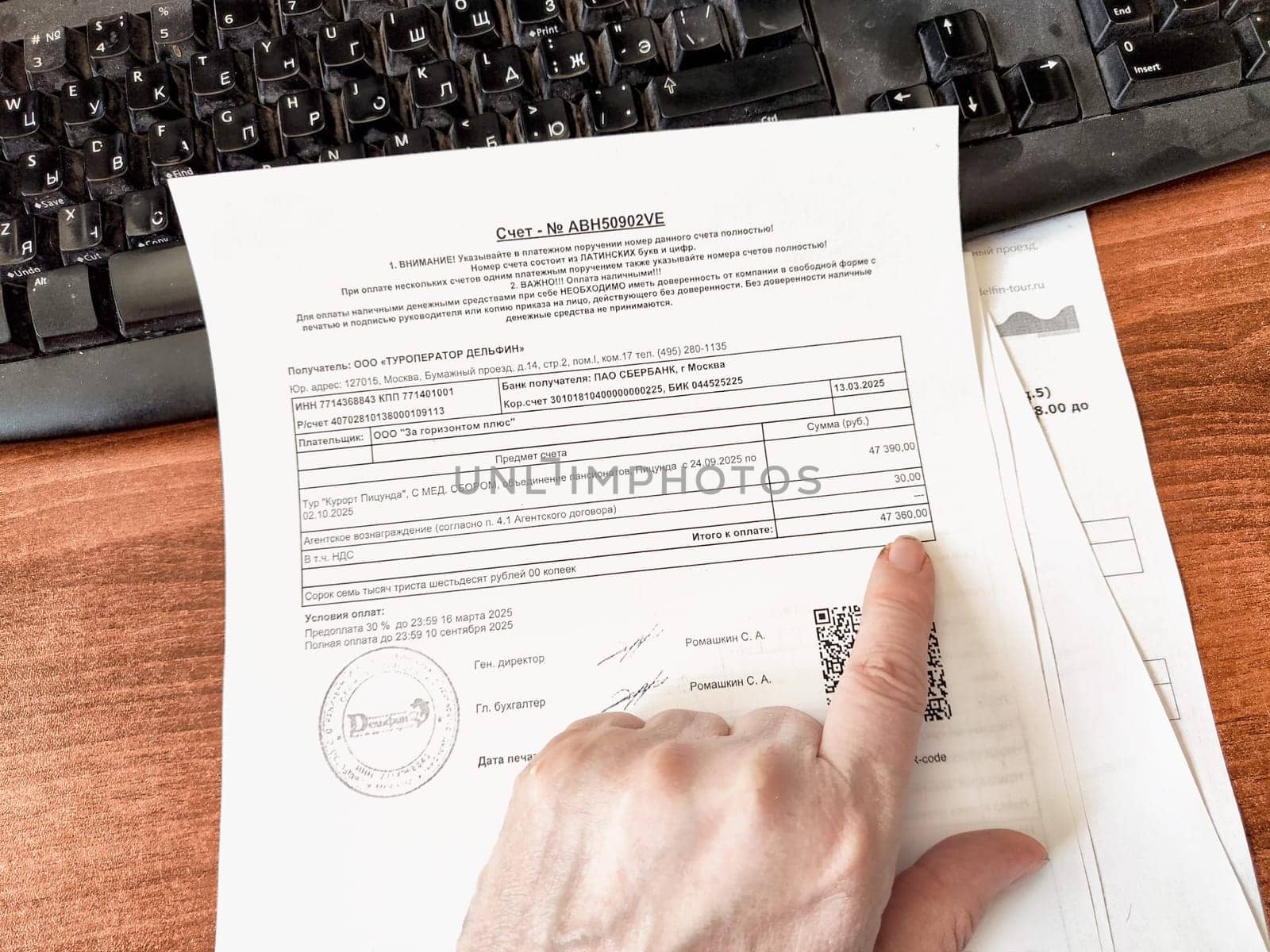 Kirov, Russia - March 18, 2025: A hand points at a payment receipt on a cluttered desk next to a computer keyboard, indicating financial transactions.