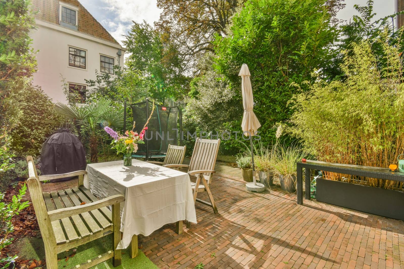 a patio with chairs, tables and umbrellas on the table in front of a house surrounded by lush green trees