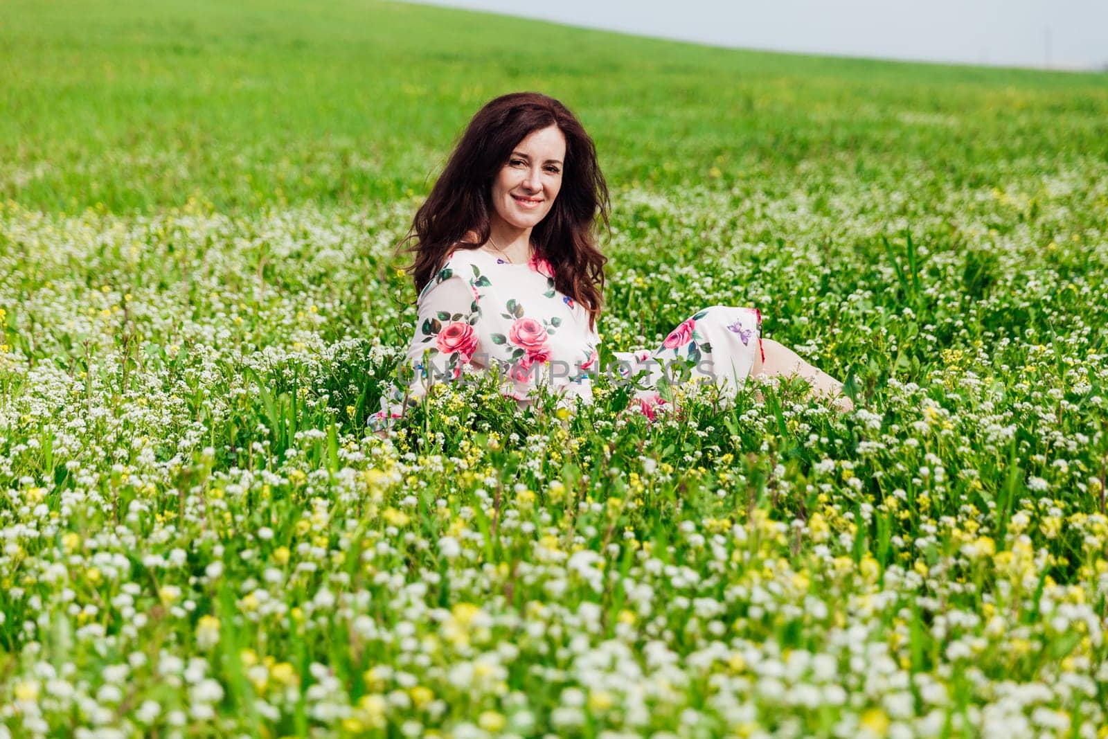 Brunette woman sitting in a field with flowers in spring and smiling