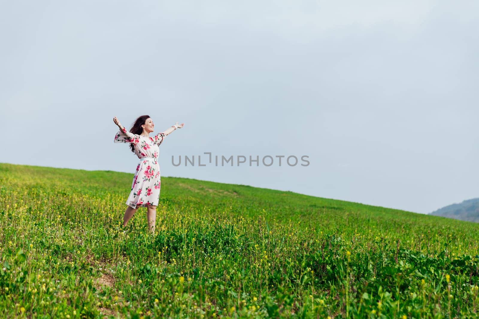 brunette woman standing with her arms outstretched in a field of flowers in spring and smiling