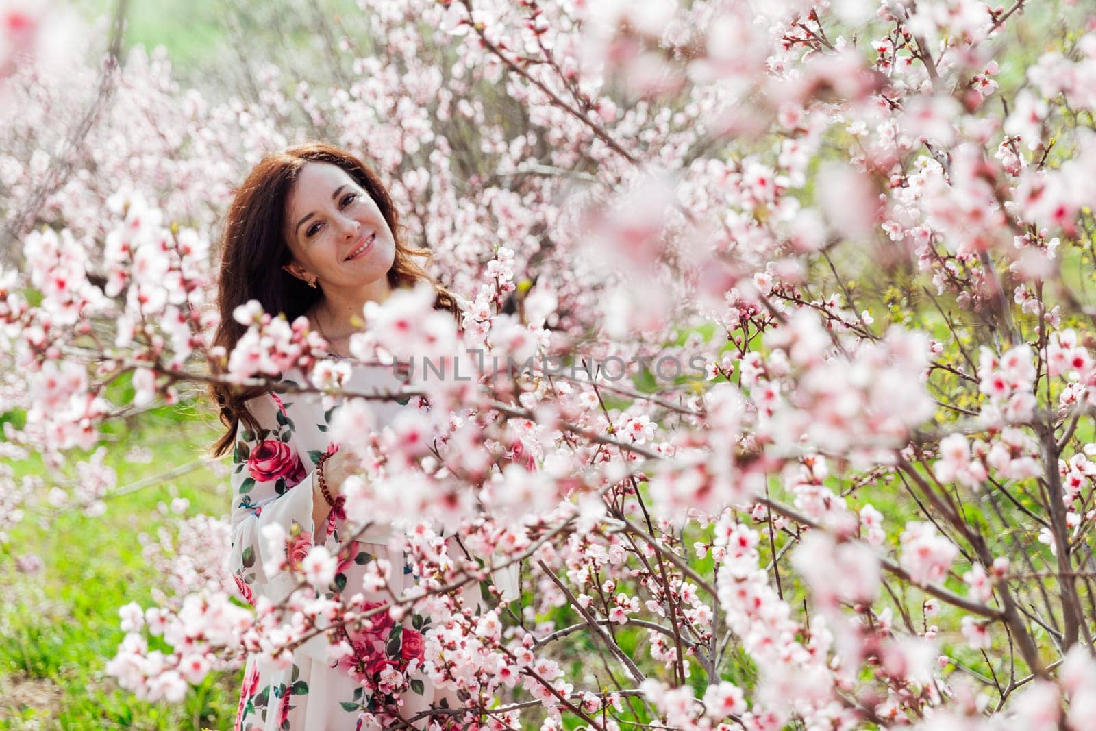 Brunette woman walking in flower dress in spring blooming garden