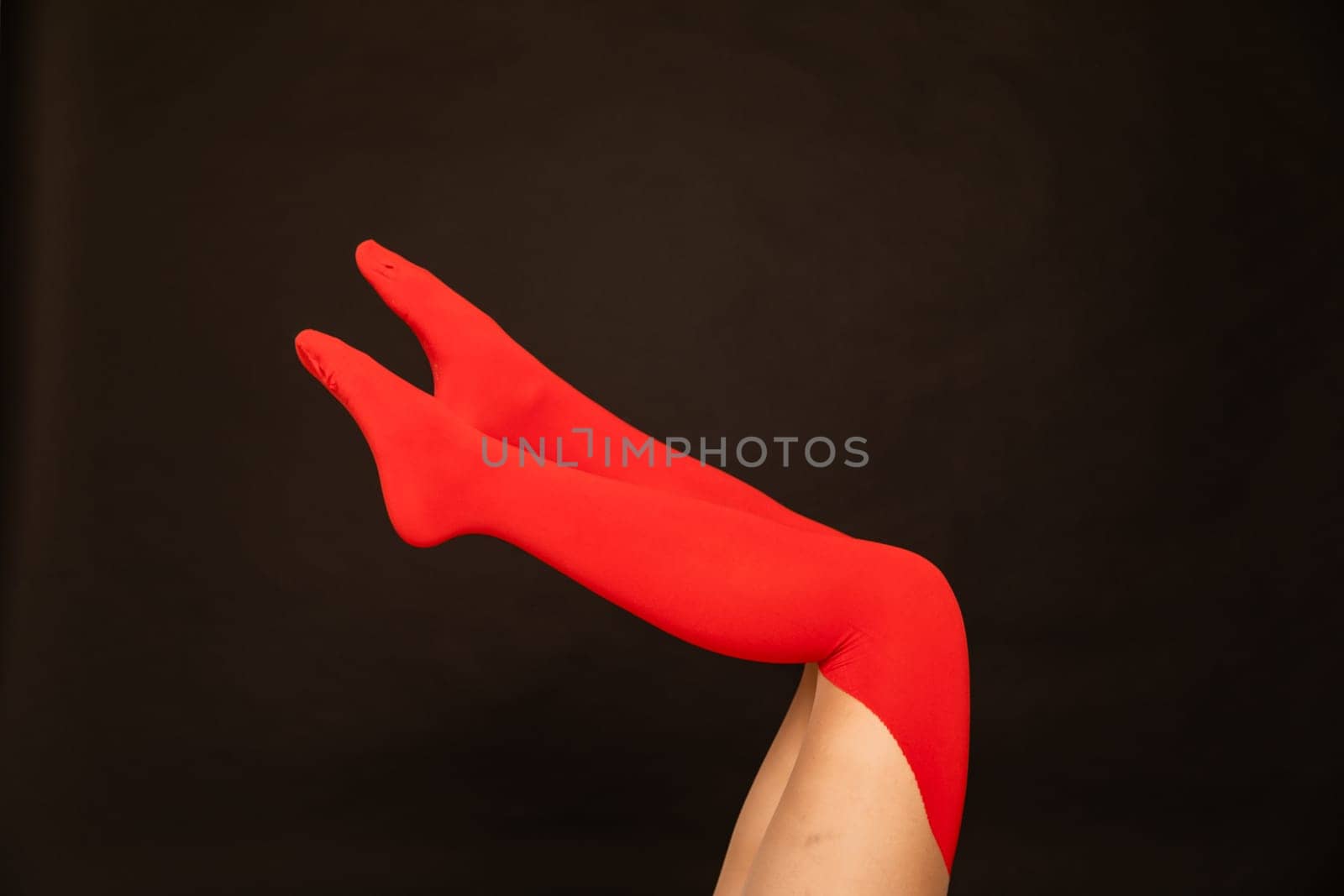 Slender female legs in red stockings, tights on a black background