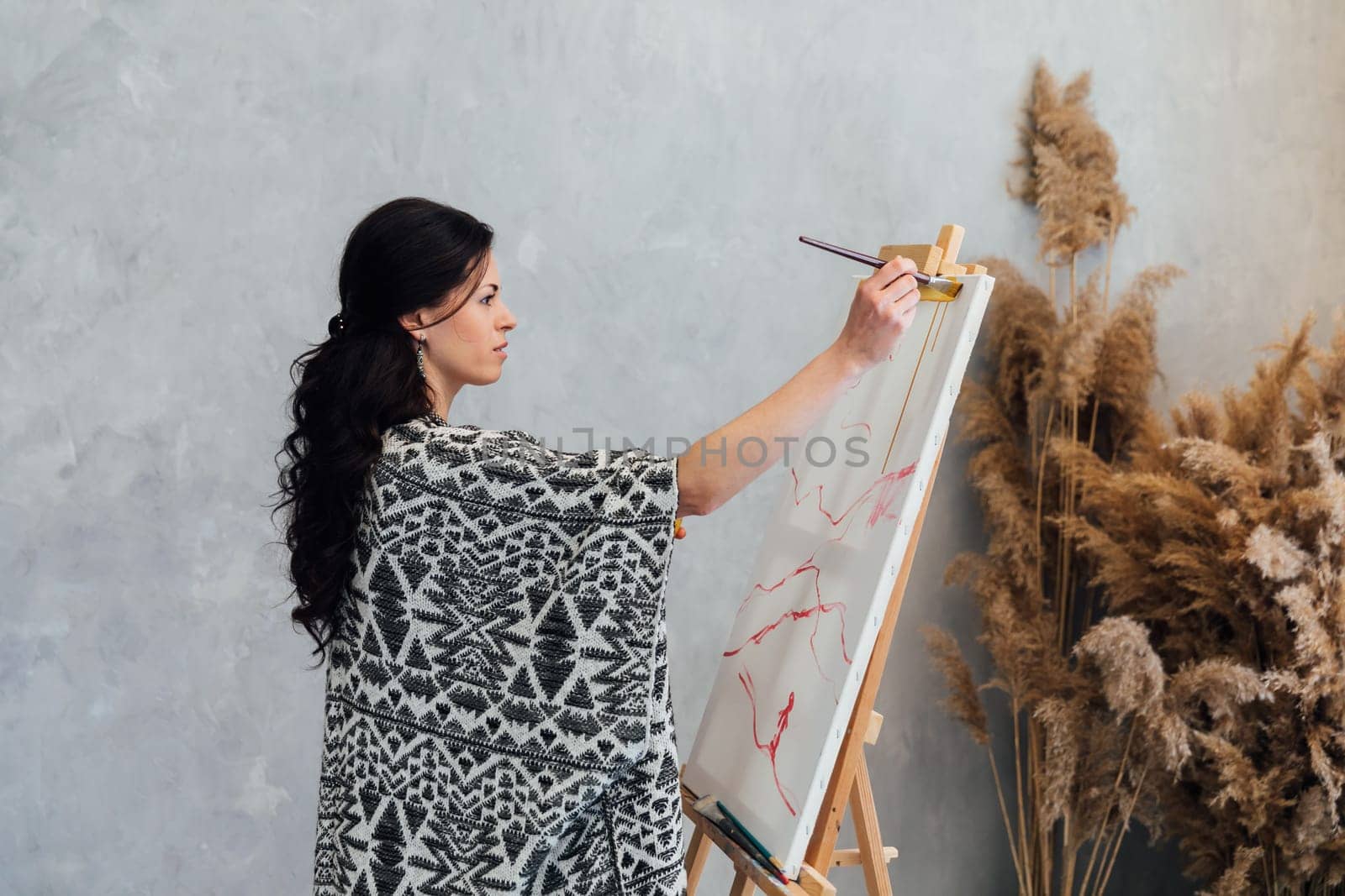 Brunette artist painting a picture on an easel with a brush with paints