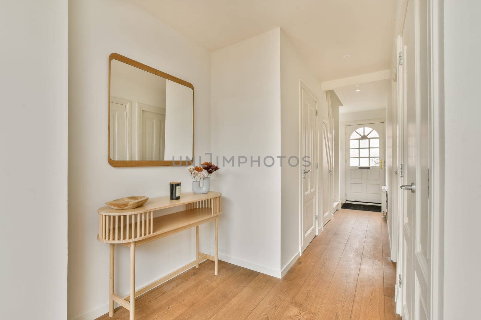 A sleek and bright hallway featuring a wooden floor, white walls, a stylish mirror, and minimal decor, radiating a fresh, airy ambiance.