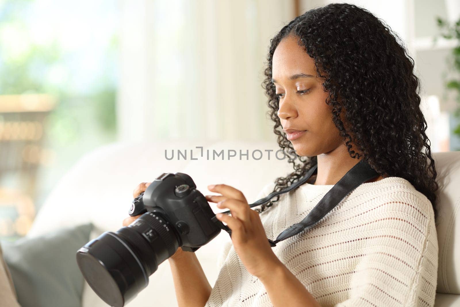 Serious black photographer at home checking dslr camera