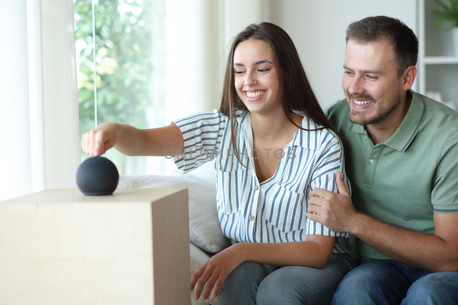 Happy couple starting new smart speaker sitting on a couch at home