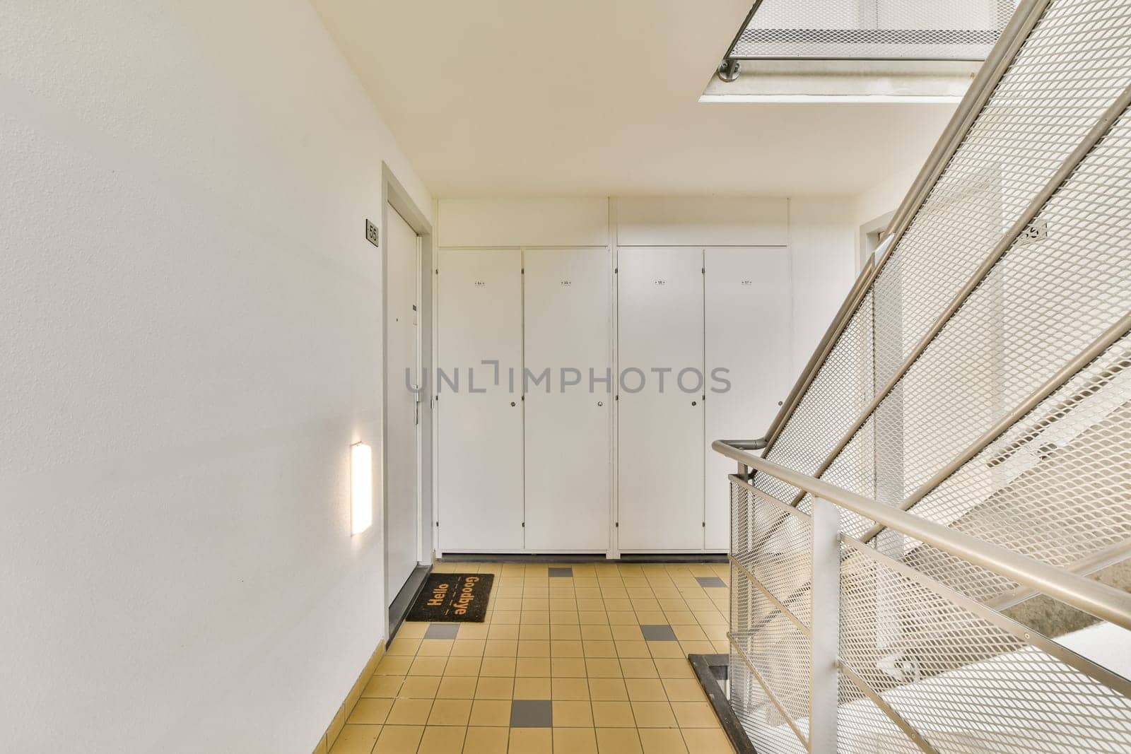 A sleek indoor corridor featuring contemporary design elements including a staircase and storage lockers along the walls, illuminated by natural light.