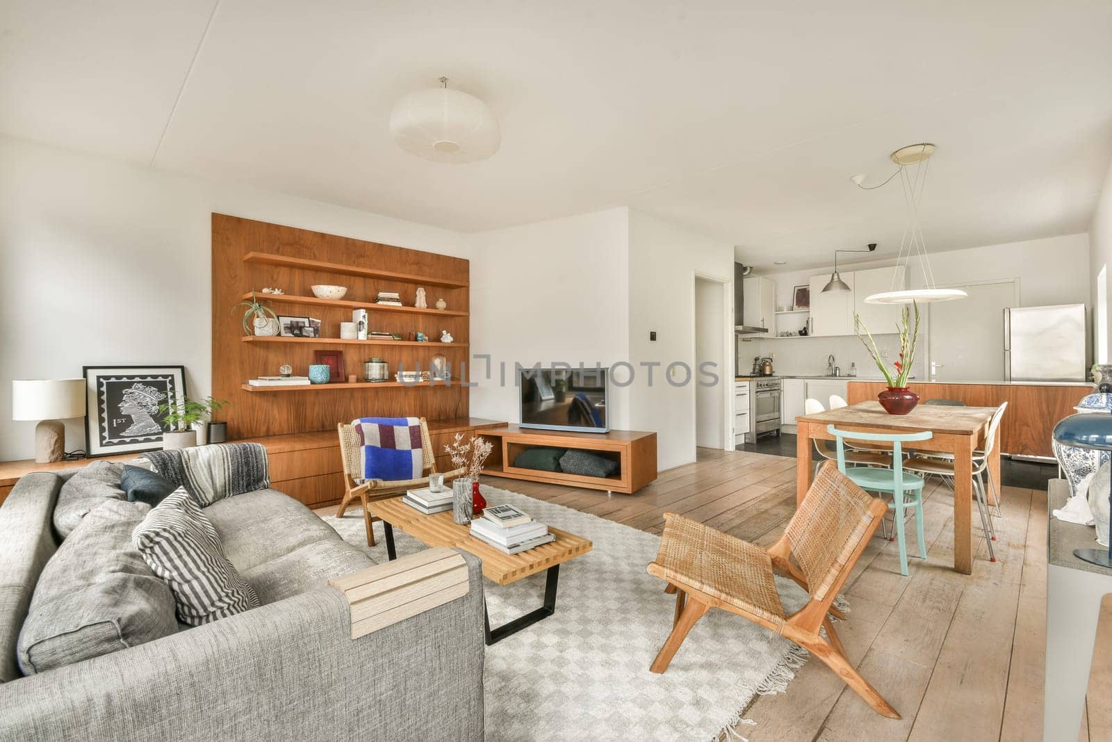 A stylish modern living room featuring a cozy sofa and adjacent dining area. The space showcases minimalist decor with warm wood accents and ample natural light.