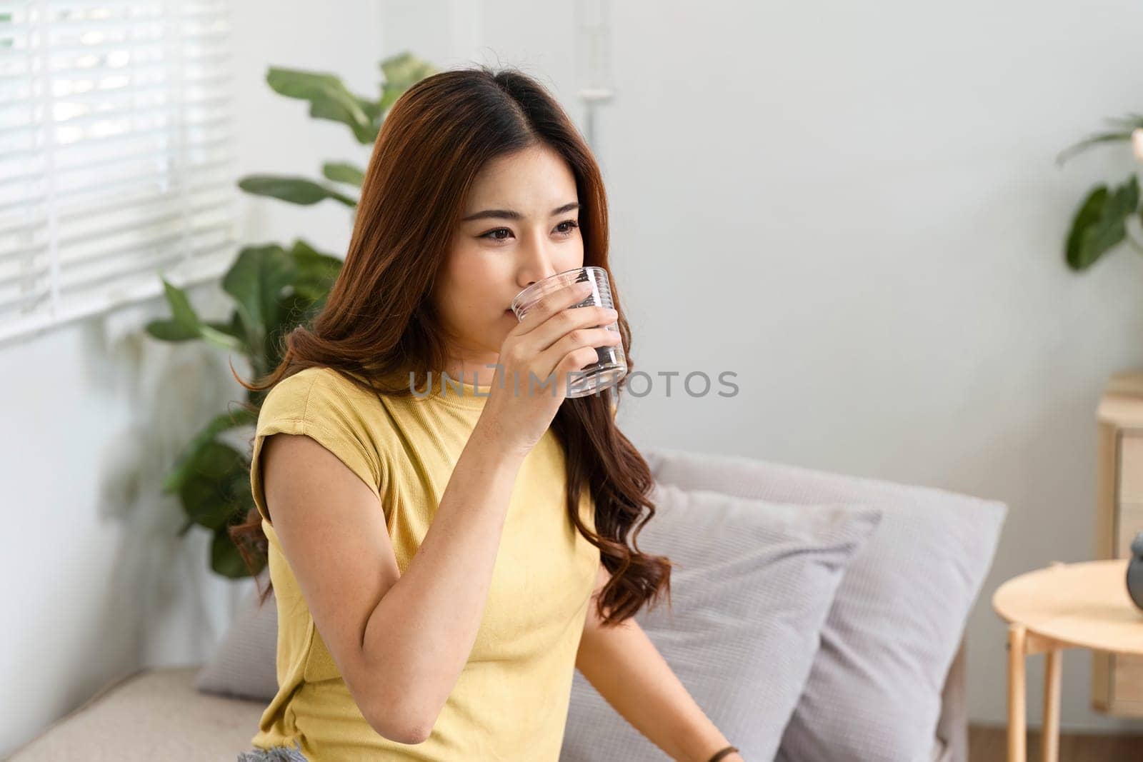 After waking up, a woman takes a moment to hydrate with a glass of water, emphasizing the importance of wellness in her morning routine.