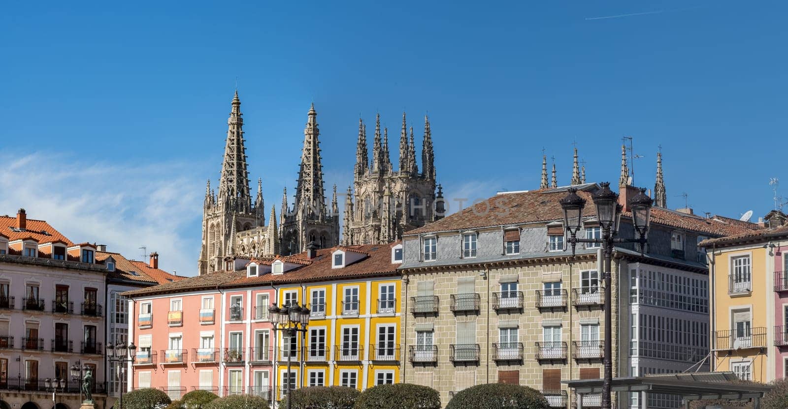 A vibrant cityscape features a historic Gothic cathedral, dominating the skyline, amidst colorful traditional buildings.