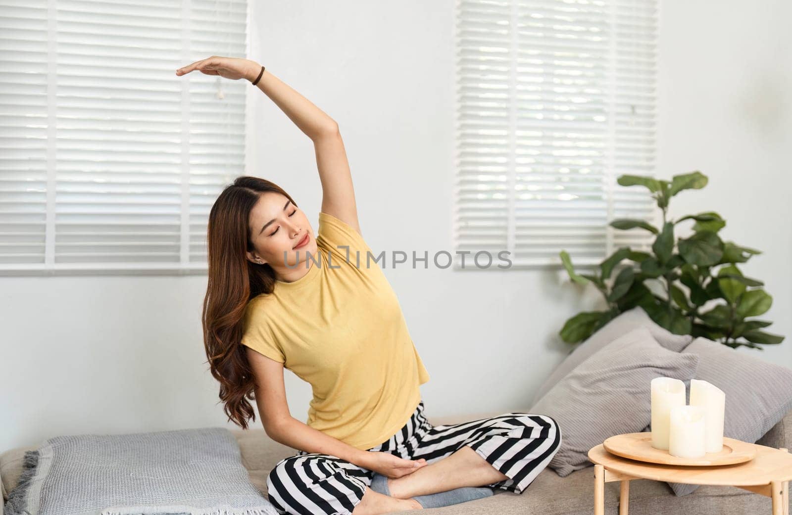A young woman performs gentle stretching on her couch, promoting health and well-being as part of her morning routine.