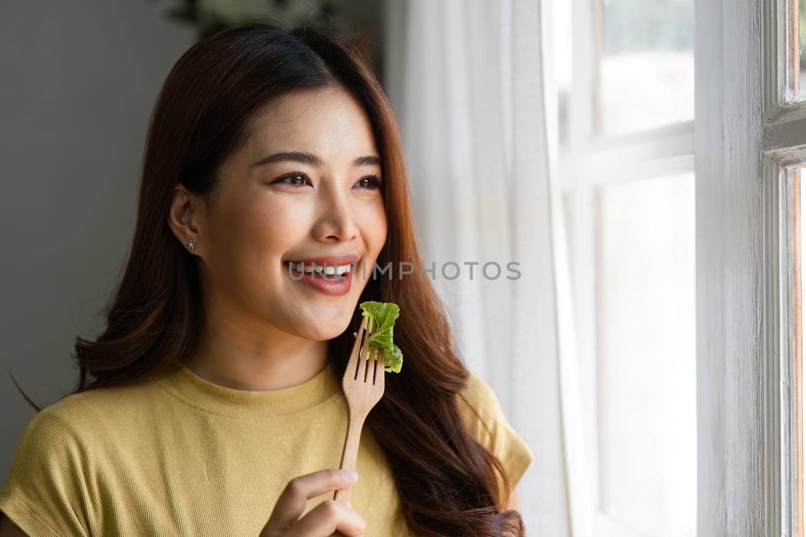 In a moment of inspiration, a woman enjoys her fresh salad while gazing out the window, reflecting a harmonious morning in her healthy lifestyle.