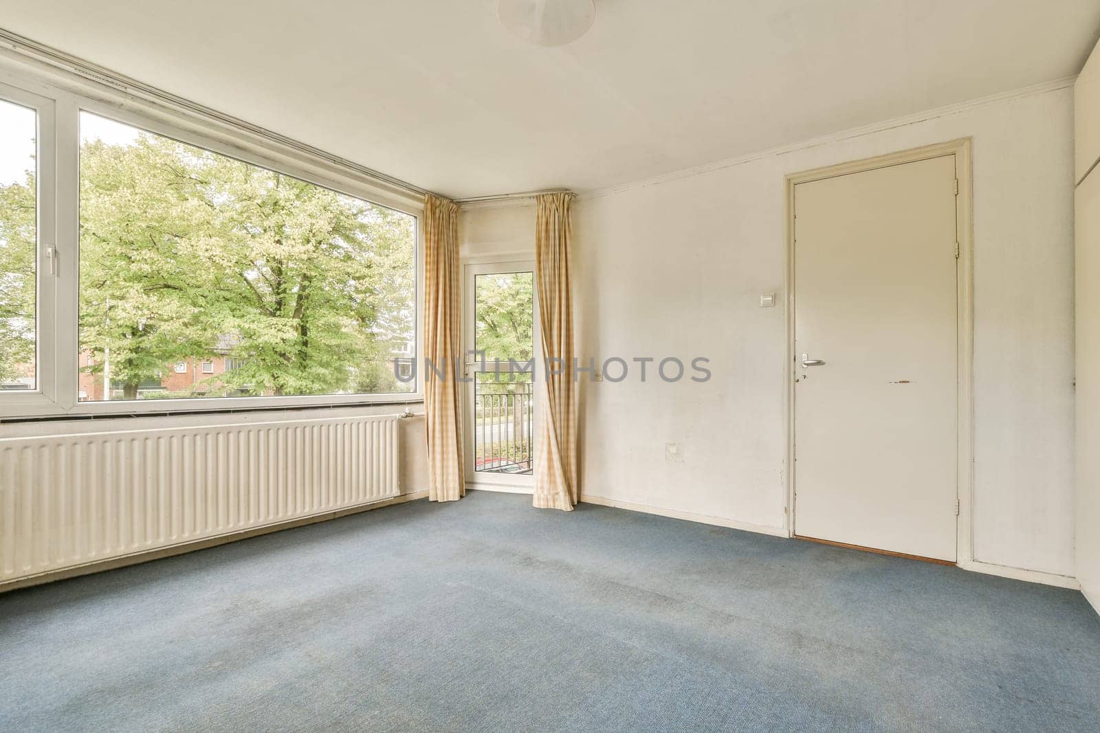 A bright room featuring large windows that allow natural light to fill the space, complemented by light-colored walls and simple decor.