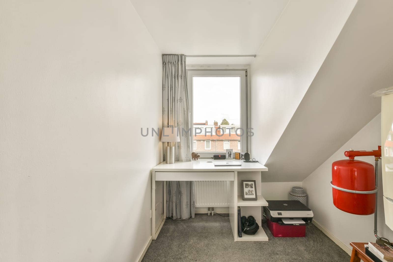 A compact workspace features a modern desk, a window bringing in natural light, and minimal decor for a clean and neat ambiance.