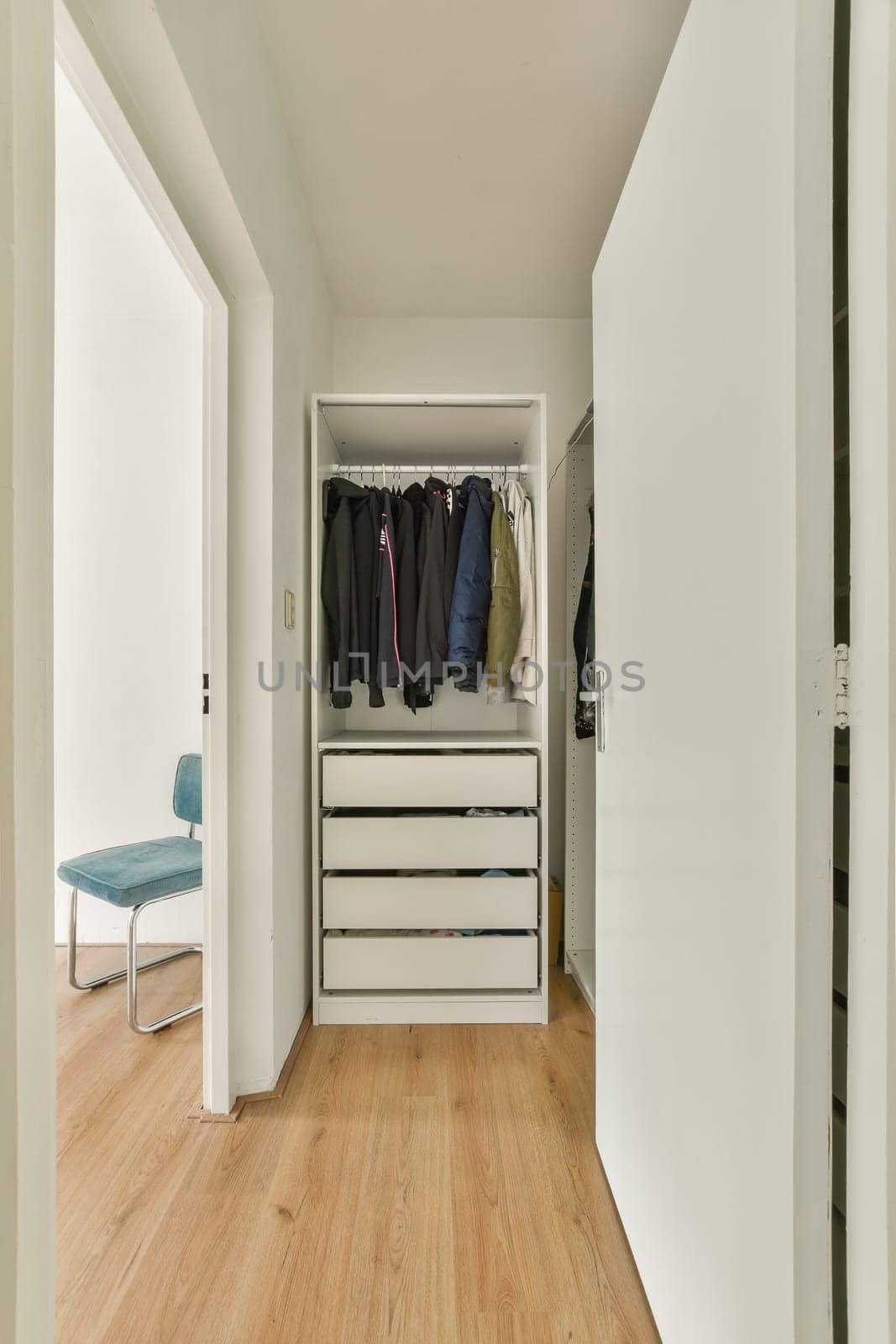A tidy and modern interior featuring a wardrobe with clothes and a simple chair. The design emphasizes minimalism and functionality.