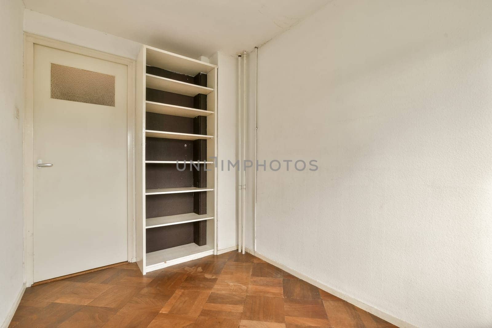 A simple interior space featuring a light-colored wall, wooden flooring, and a narrow shelf against the wall, creating a clean and uncluttered appearance.