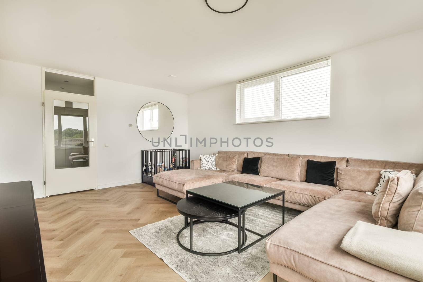 A stylish modern living room featuring a cozy sofa, coffee table, and large windows allowing natural light. The wooden flooring adds warmth to the space.