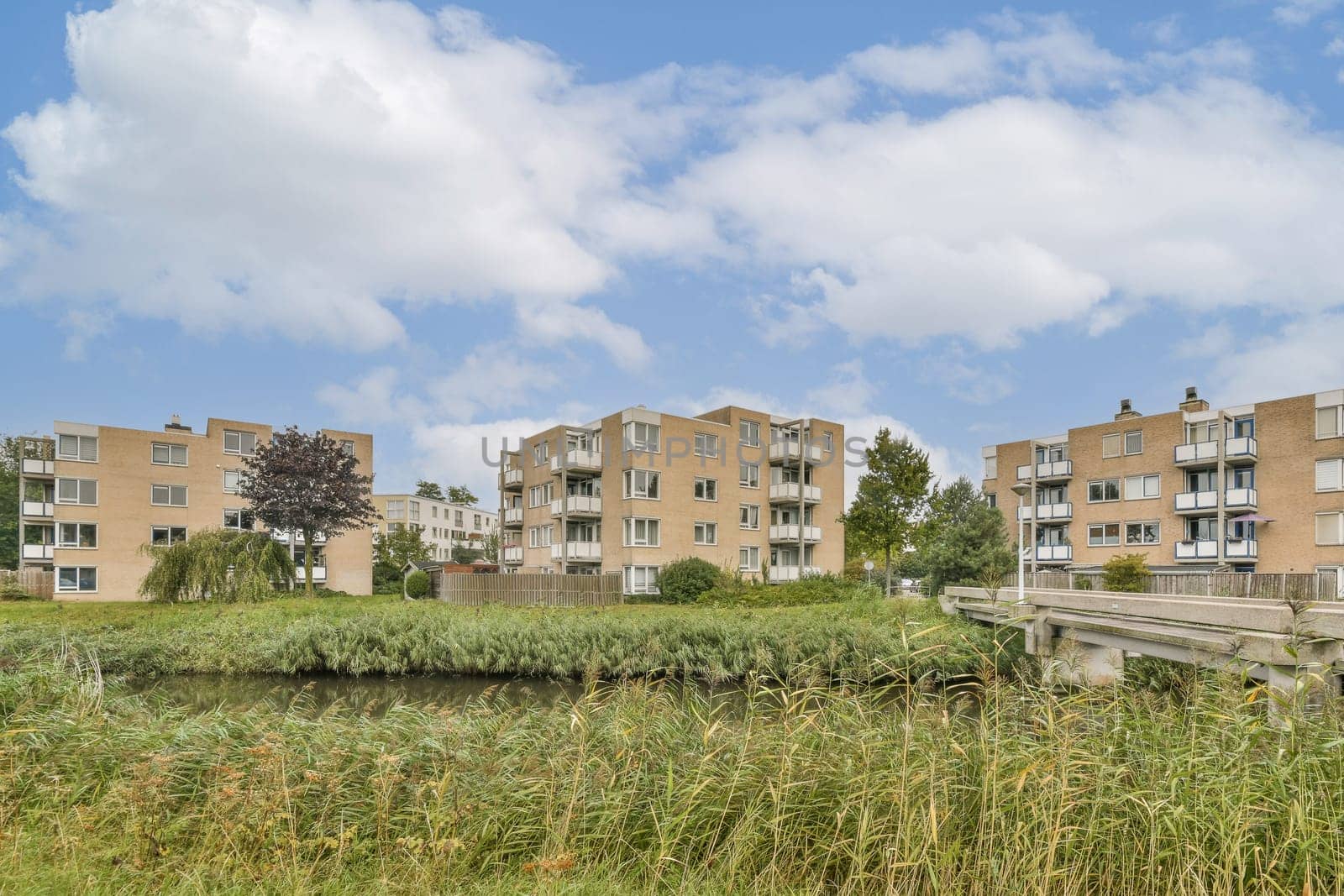 Contemporary apartment complexes surrounded by lush greenery and a calm waterway, showcasing an idyllic living environment amidst nature.
