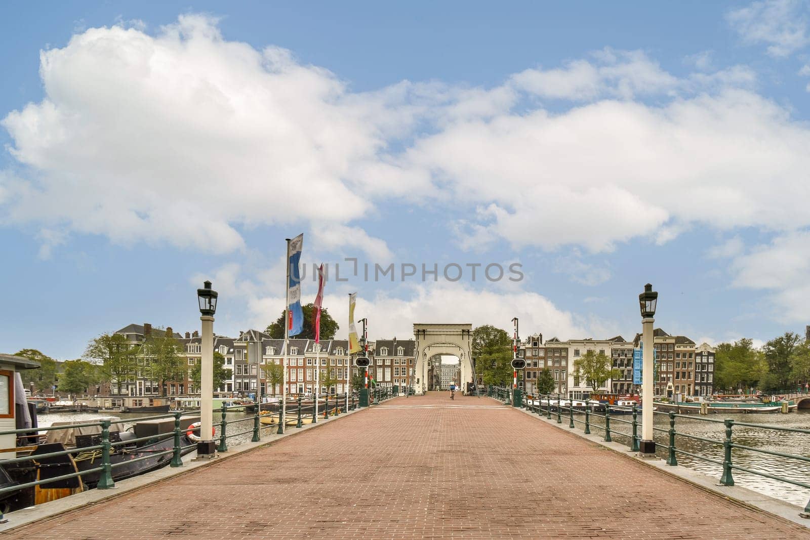 A picturesque view of a waterfront pathway leading towards historic buildings under a vibrant sky, capturing the charm of Amsterdam's architecture.