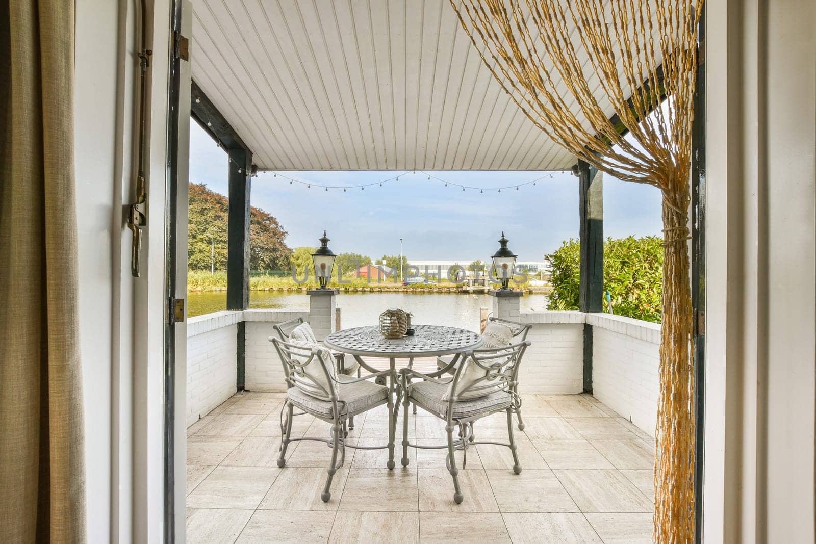 An inviting outdoor patio featuring a round table and chairs, surrounded by lush greenery and decorative lanterns, perfect for relaxation and gatherings.