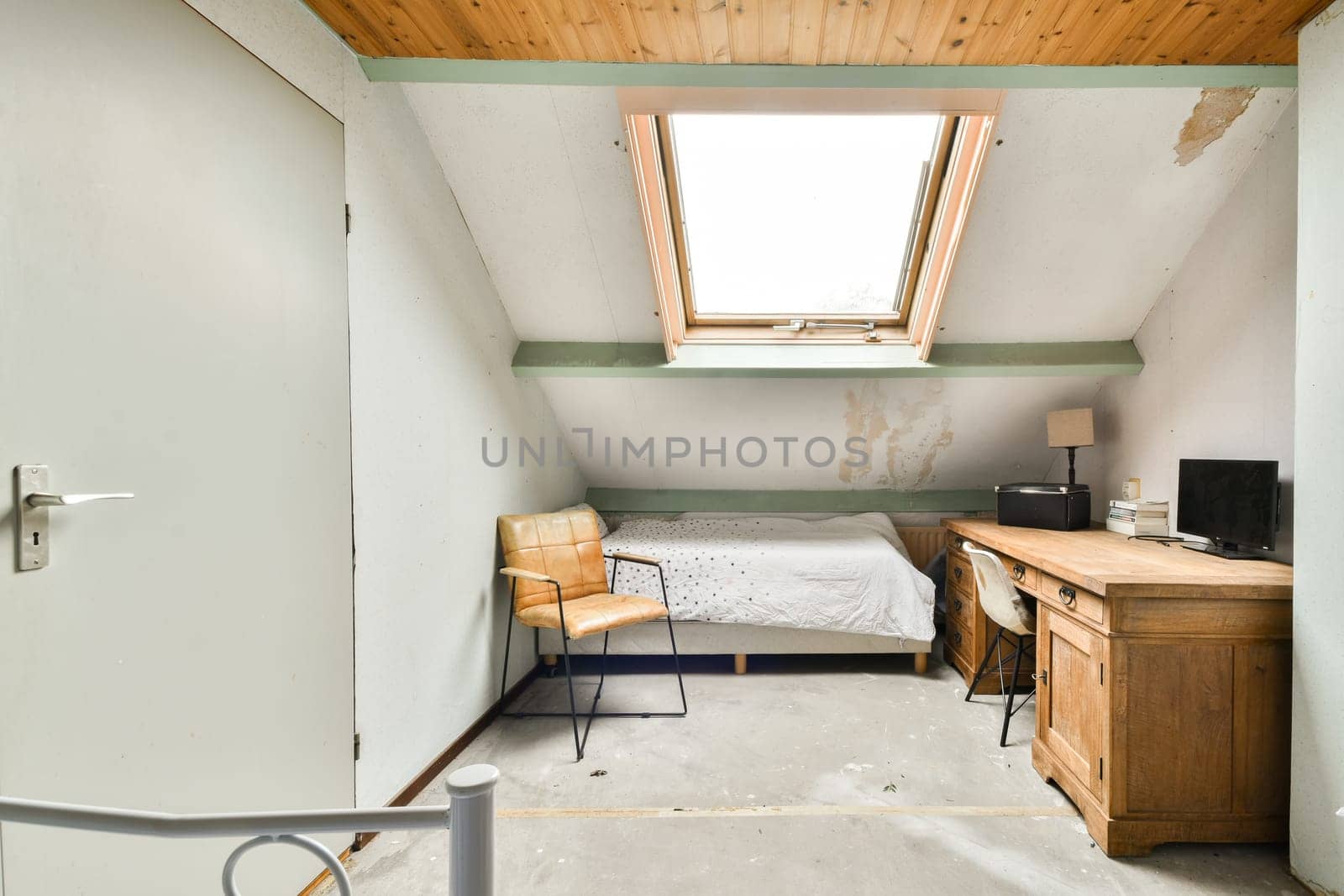 A simple yet elegant bedroom featuring a bed, desk, and chair, illuminated by natural light streaming through a skylight. The design is uncluttered and calming.