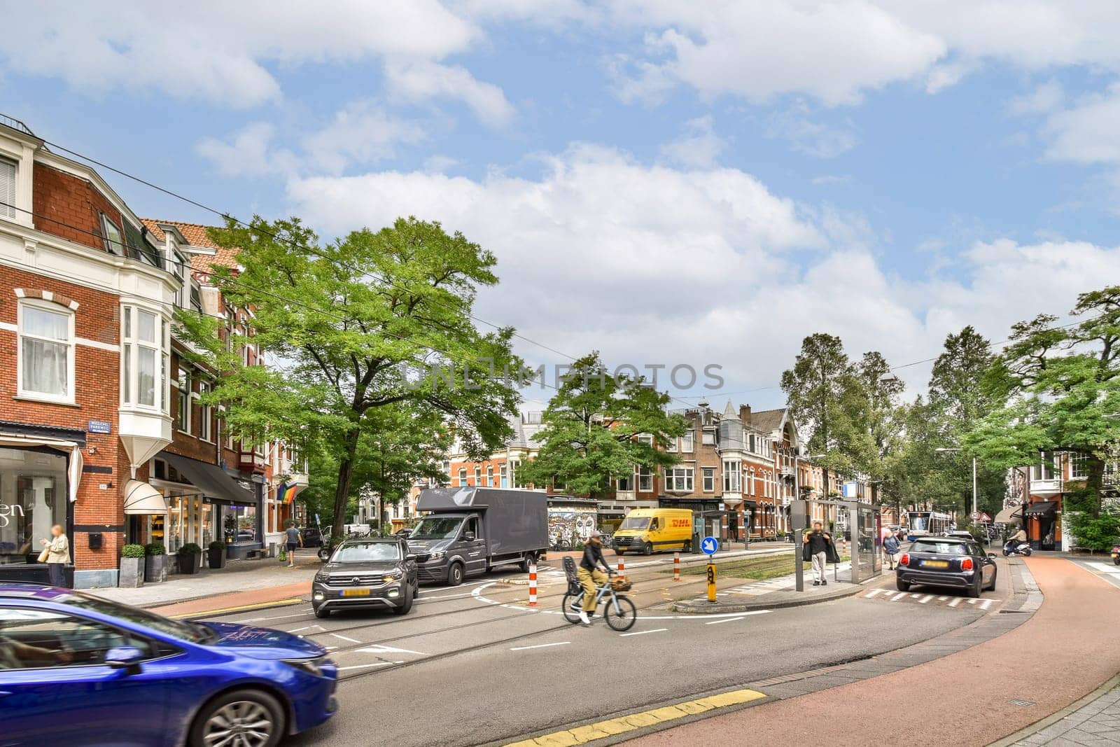 A lively urban street featuring busy traffic, green trees, and pedestrians, showcasing modern city life and architecture under a clear sky.